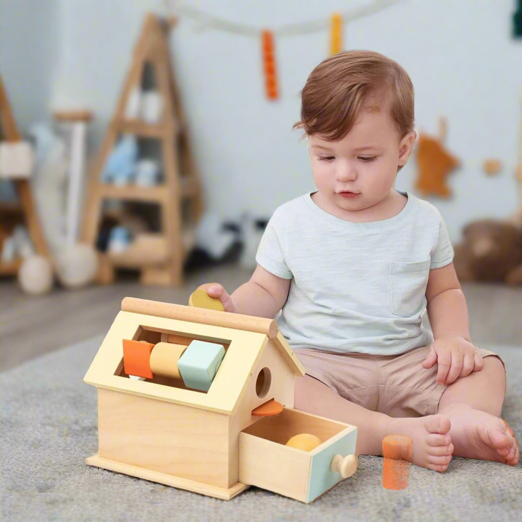 Baby boy playing on the carpet of his nursery room with a 4 in 1 wooden Montessori toy house