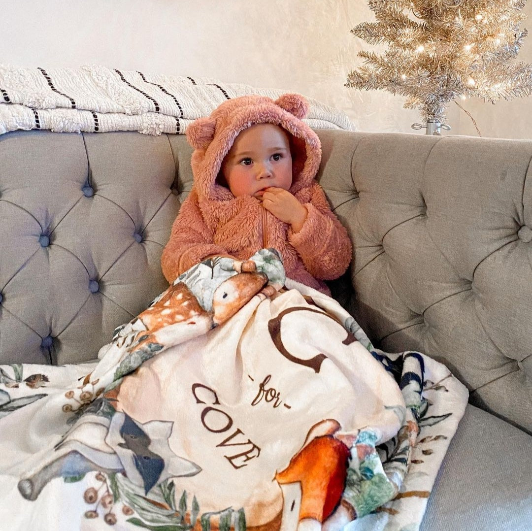 Baby girl sitting in the living room covered with her warm fleece personalized baby blanket