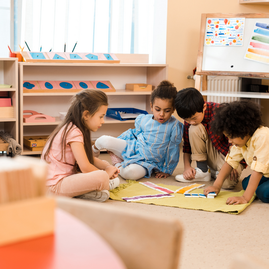 Group of four children playing with a puzzle and wooden blocks on the floor of a classroom.