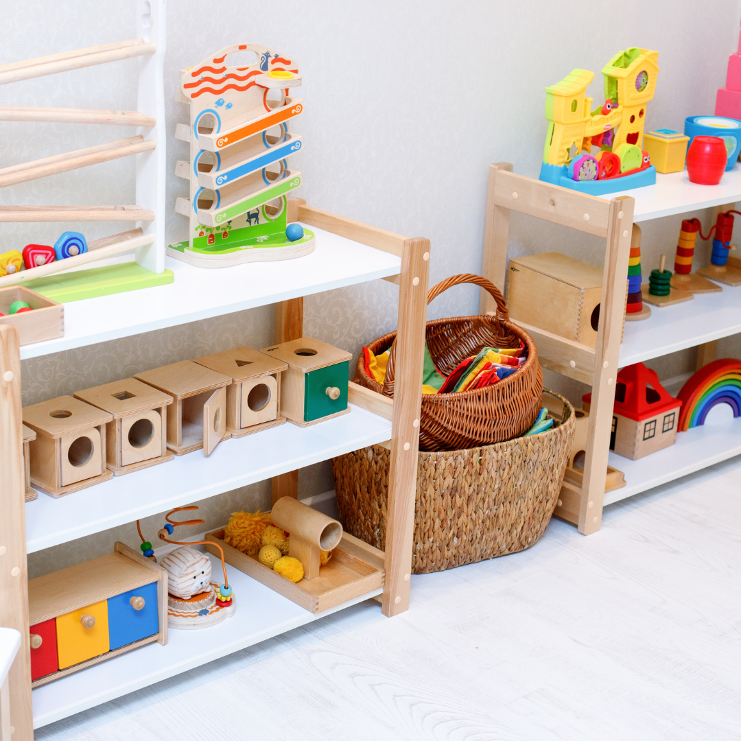 two white wooden shelves displaying many wooden toys on them and two baskets on the floor with books and activities.