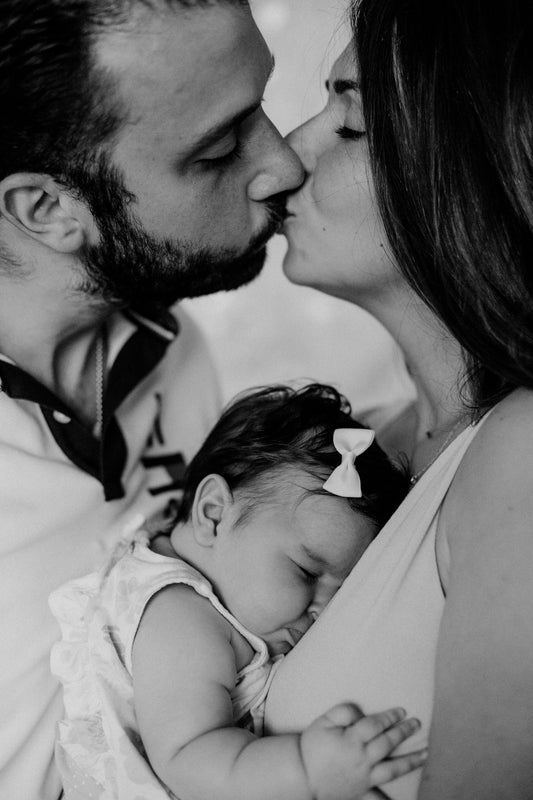 two parents kissing and holding their new baby girl in their arms.