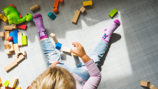 Little girl playing with colorful wooden block on the floor of her room with sunlight shining inside