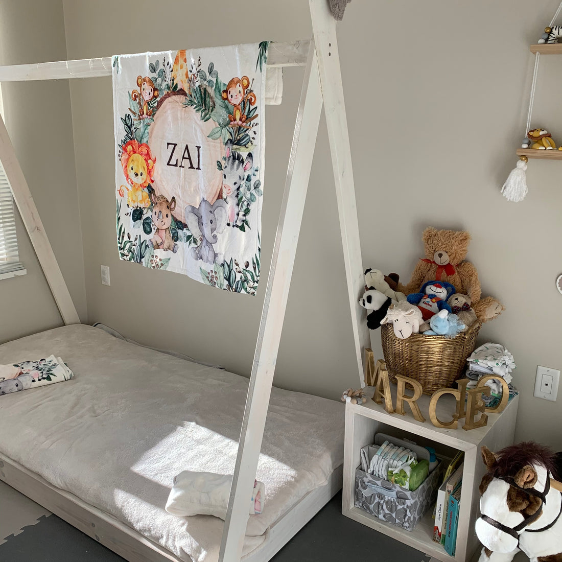 baby's nursery showing a DIY Montessori bed with a personalized baby blanket hung on it and some other decorations around