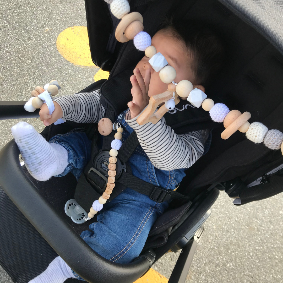 Baby in stroller holding a wooden rattle and playing with a stroller hanging toy