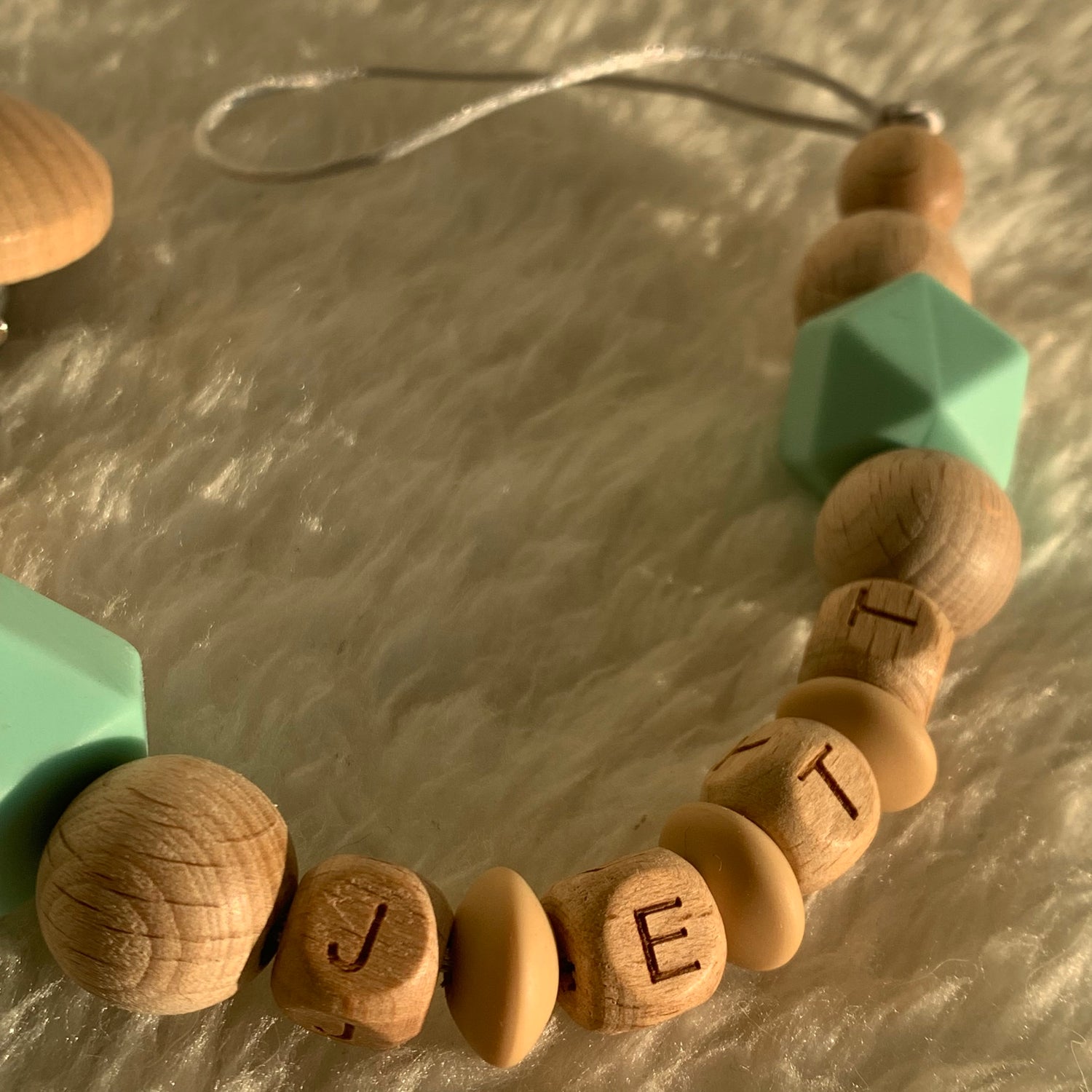 personalized wooden pacifier clip with baby's name on a fur carpet