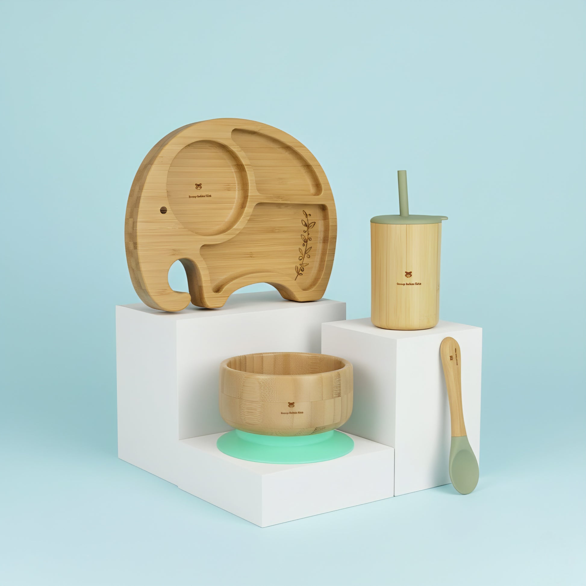 Set of bamboo baby utensils including a plate, cup, bowl, and spoon on a light blue background.