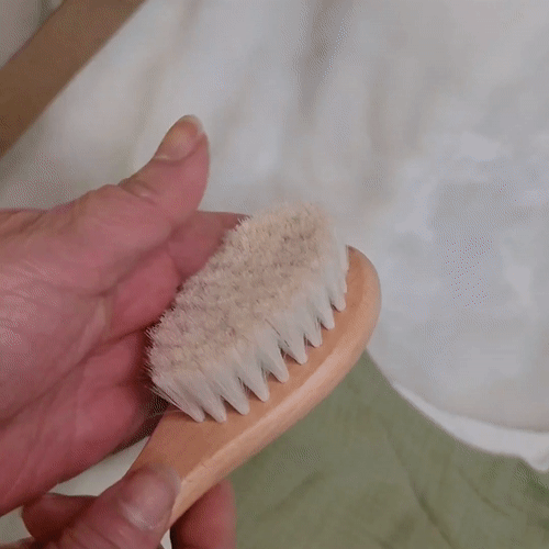 woman using her hand to show how soft the bristles of a baby hair brush is from a newborn baby gift set
