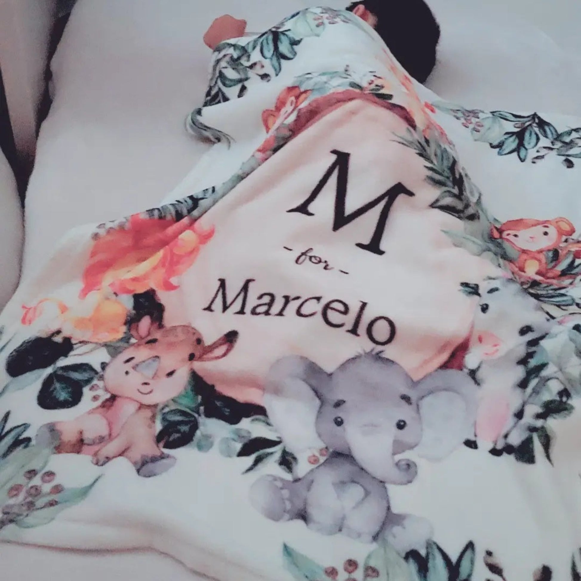 baby boy sleeping on a bed while being covered by a safari customizable baby fleece blanket with his name