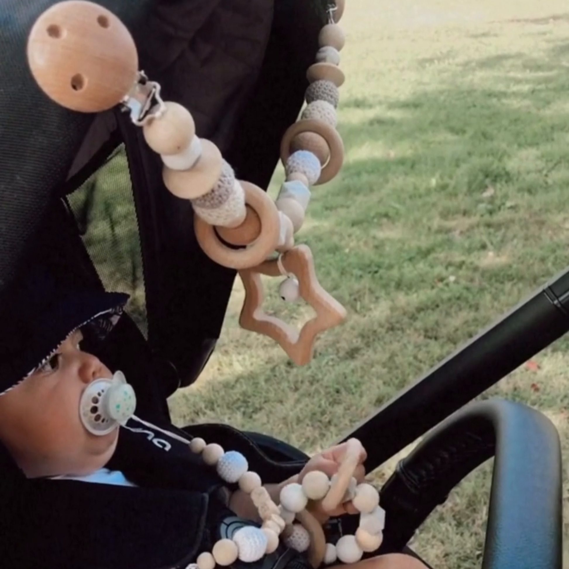 baby boy in a stroller at the park with his 3 piece wooden personalized pacifier clip 