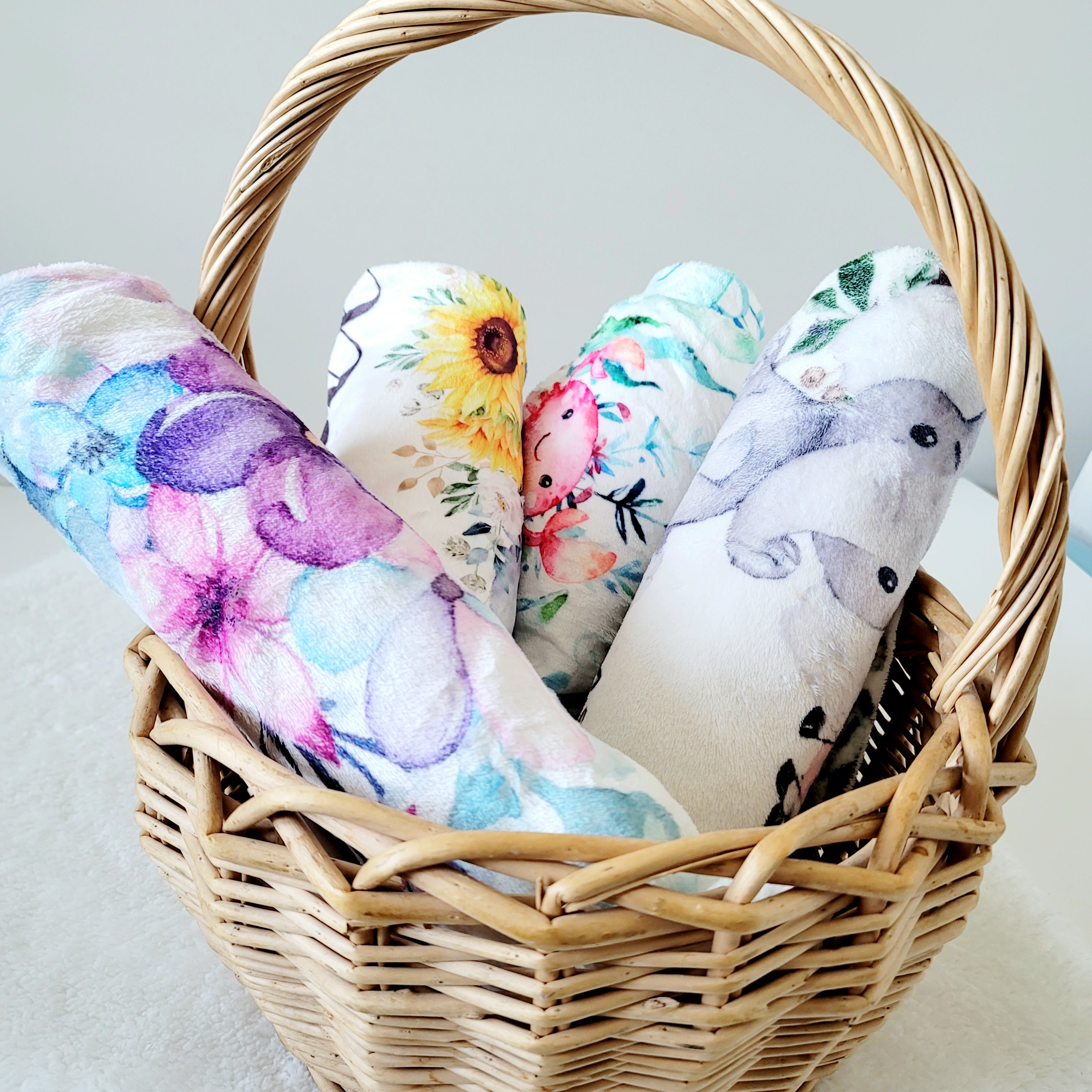 A group of four baby fleece blankets with cute designs made into rolls inside a wooden basket.