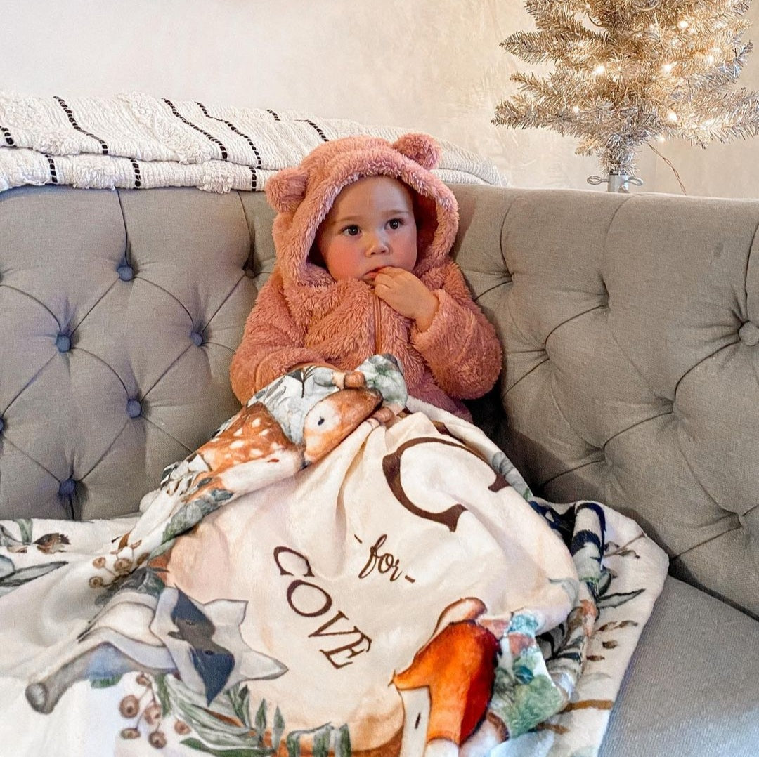 Baby girl sitting in the living room covered with her warm fleece personalized baby blanket 