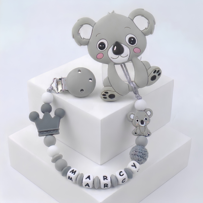 Gray koala-shaped teether with matching customized soother clip with baby's name on a white background