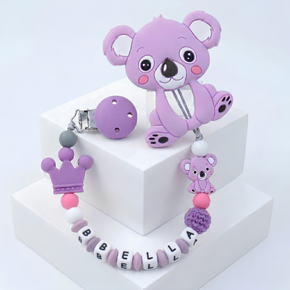 Purple koala-shaped teether with customized soother clip with baby's name on a white background