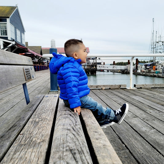 toddler boy sitting on a bench wearing a bubba bear puffer jacket for kids.
