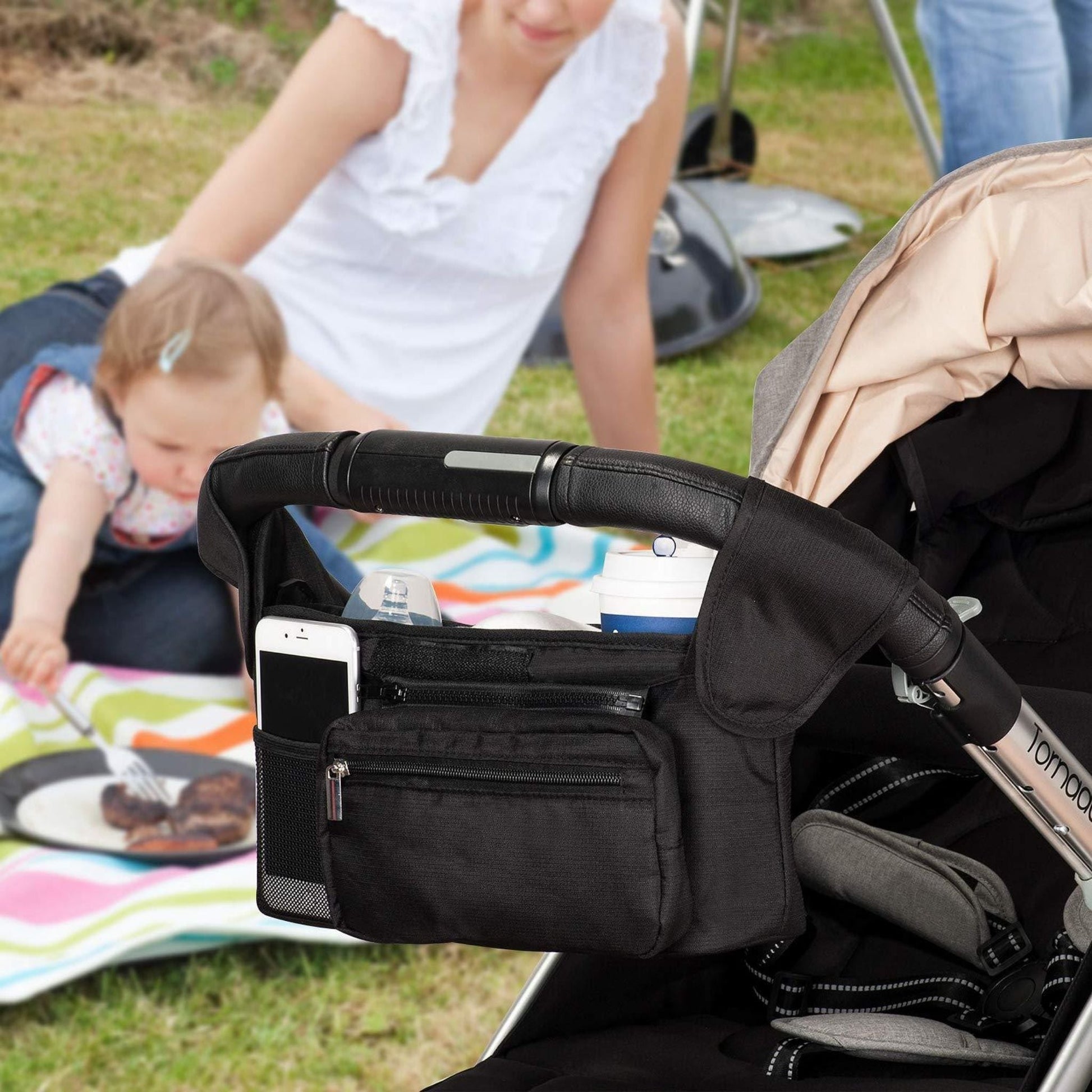 Mom at a park with her stroller and a stroller organizer and cup holder hung on it.