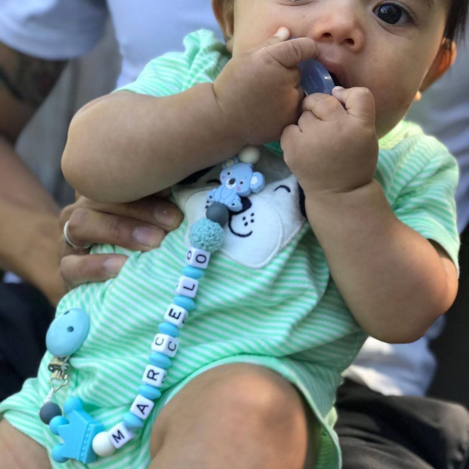 baby using the baby blue personalized pacifier clip attached to his clothes while he chews on the koala teether