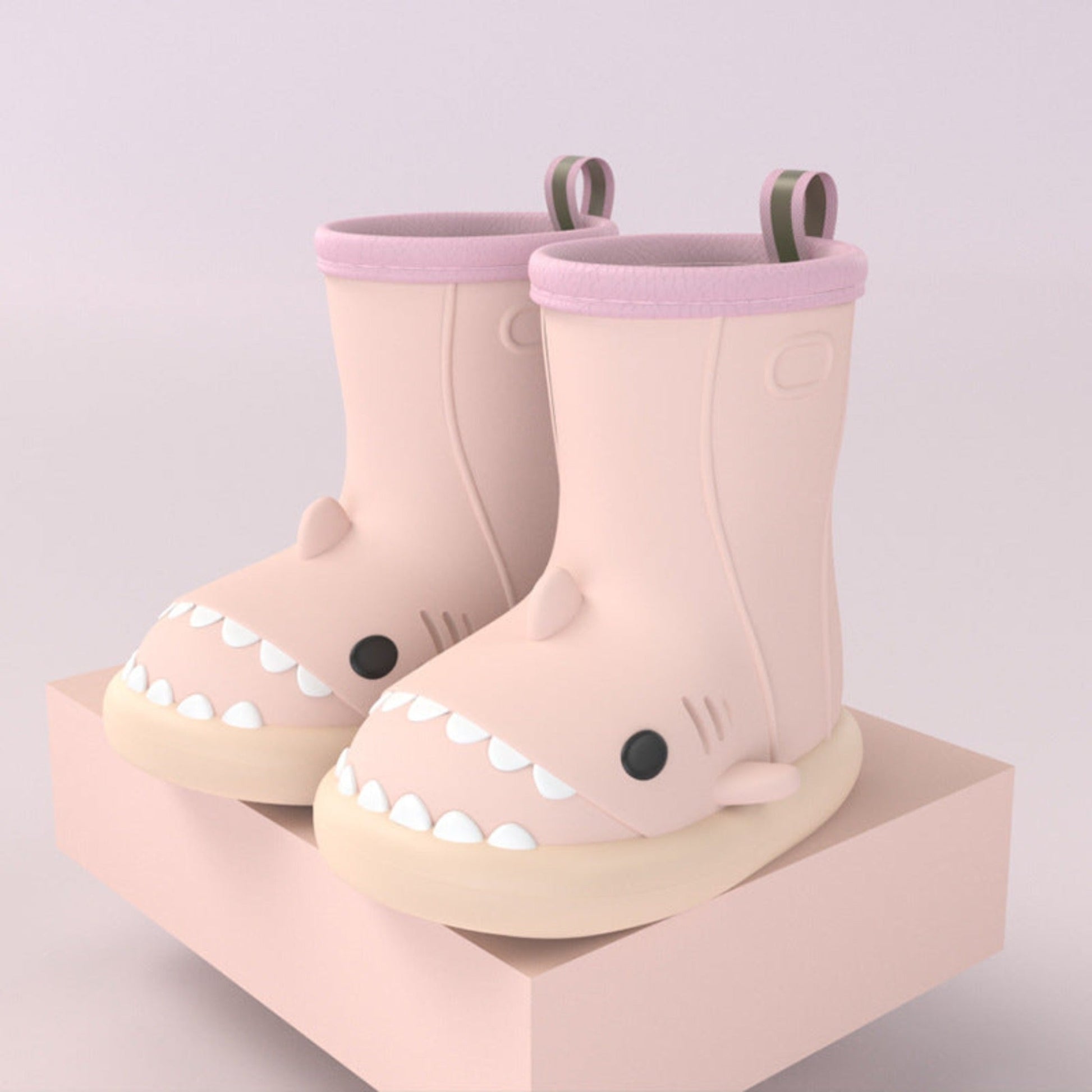 pair of pink shark rain boots for kids on a pink block for display