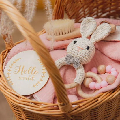 newborn baby gift set with a bunny crochet rattle, a wooden and silicone rattle, a swaddle and a bib in one basket 