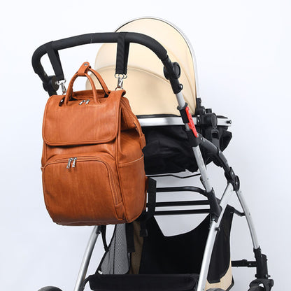 vegan brown leather diaper backpack hung with hooks from the handle bar of a stroller