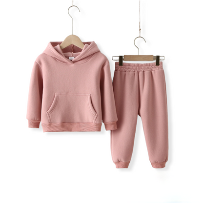 A pink warm, unisex tracksuit for toddlers and kids hung on a hanger against a white wall from hunny bubba kids