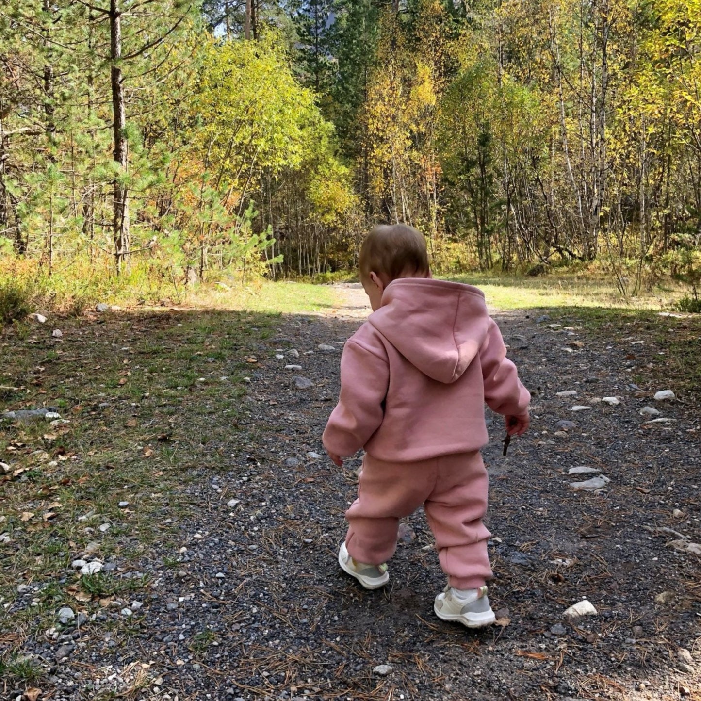 little girl walking in the forest wearing a pink tracksuit for toddlers