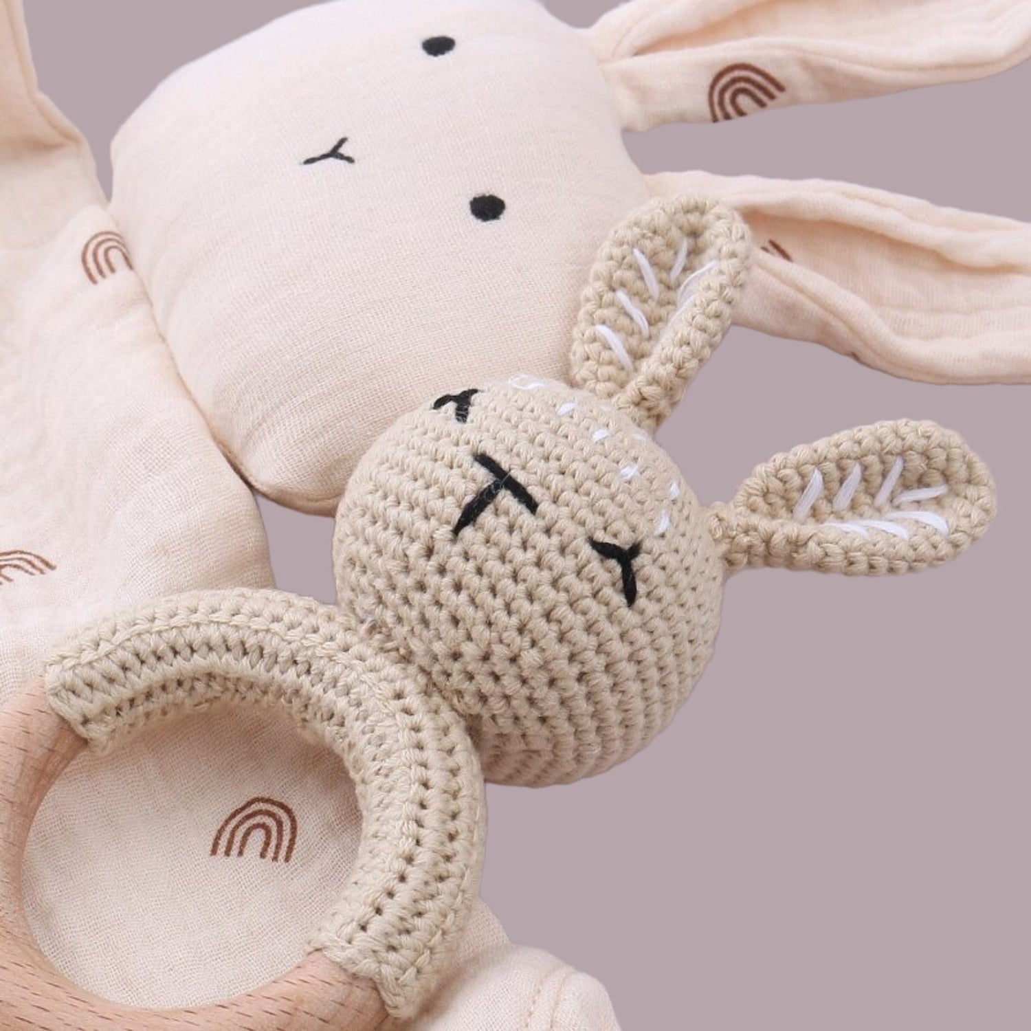 a cute beige crochet bunny rattle and a cute bunny swaddle for babies laying on a beige surface