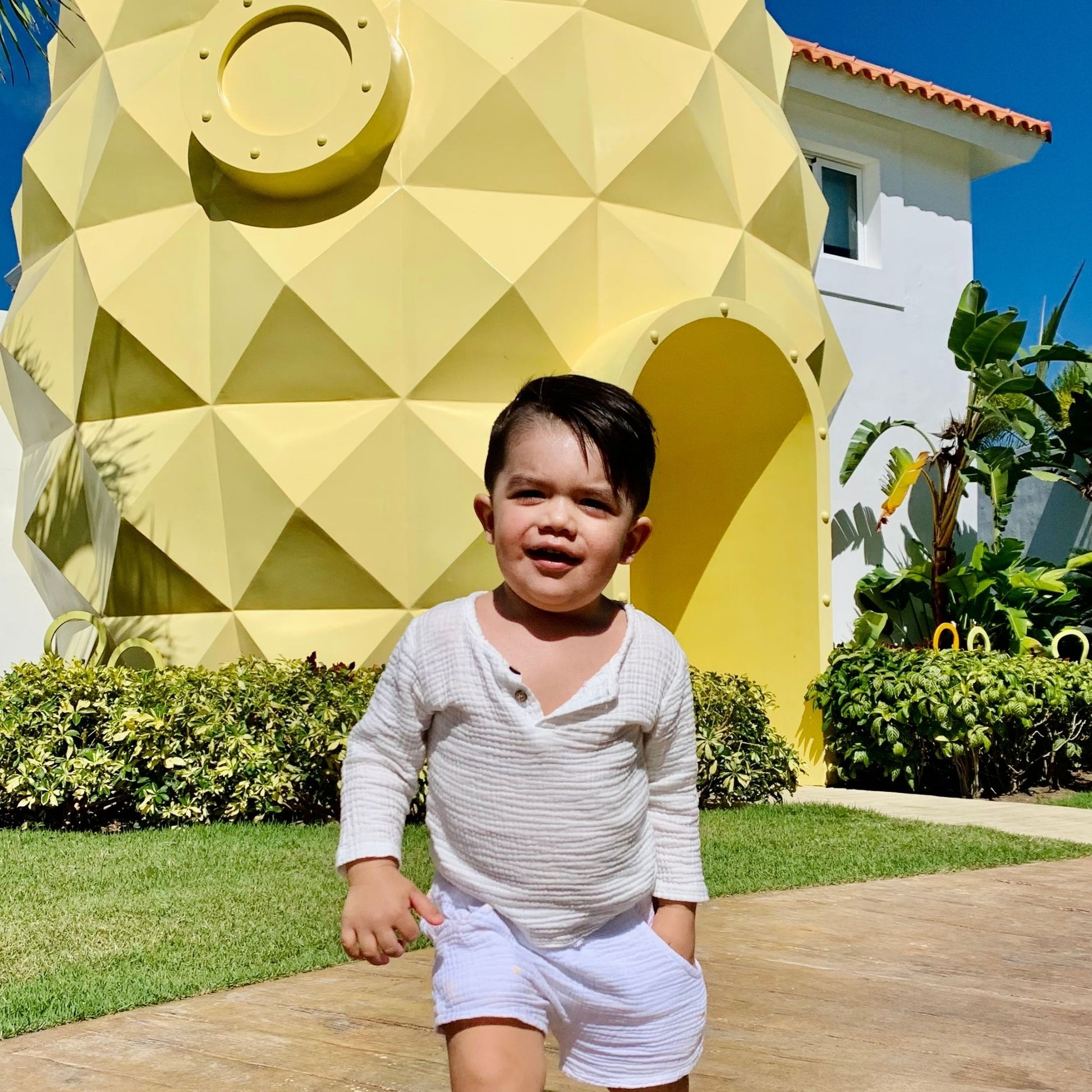 baby boy wearing a summer white sex in front of spongebob's house 